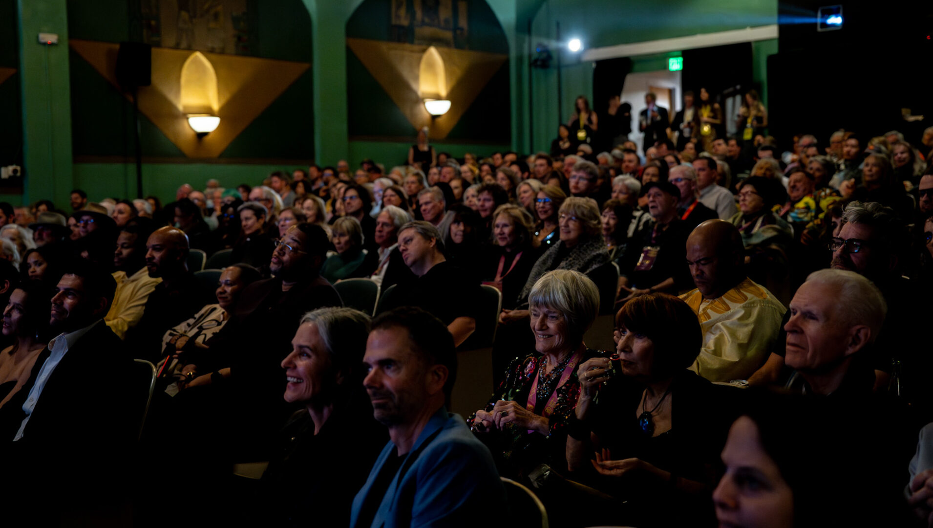 Audience seated in a dimly lit theater, attentively watching a performance