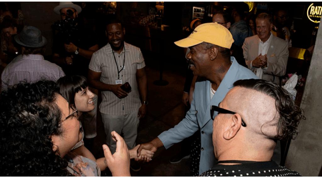 Colman Domingo smiling and shaking hands at an event, surrounded by a group of people