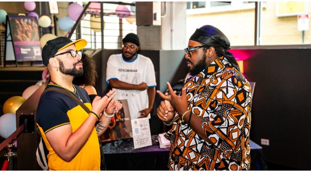 Two men conversing at an event with colorful balloons and a display in the background