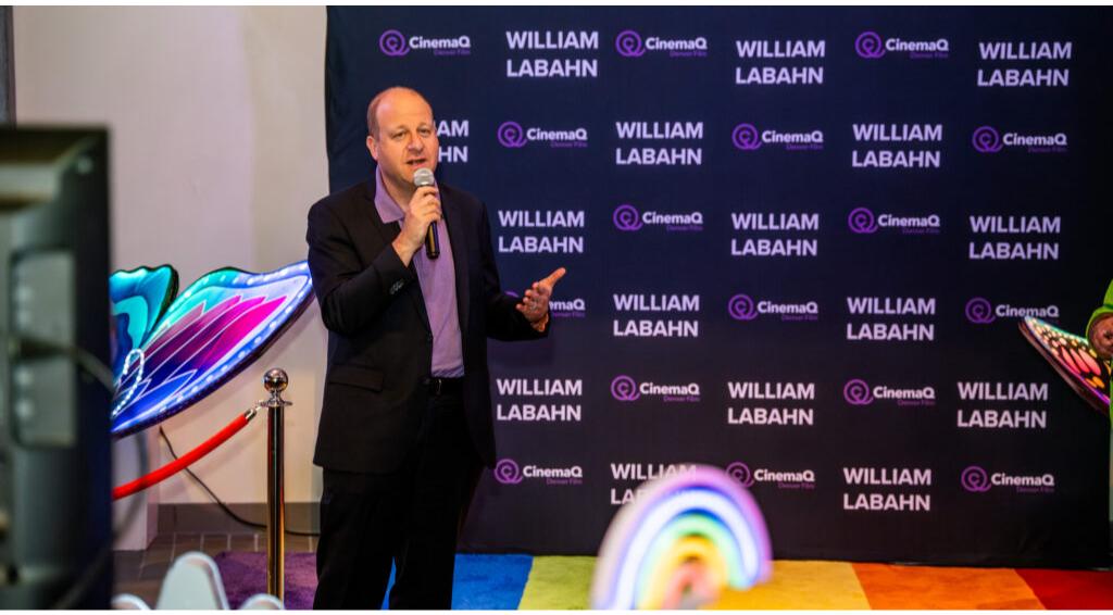 Person speaking at CinemaQ event with backdrop featuring 'WILLIAM LABAHN' text