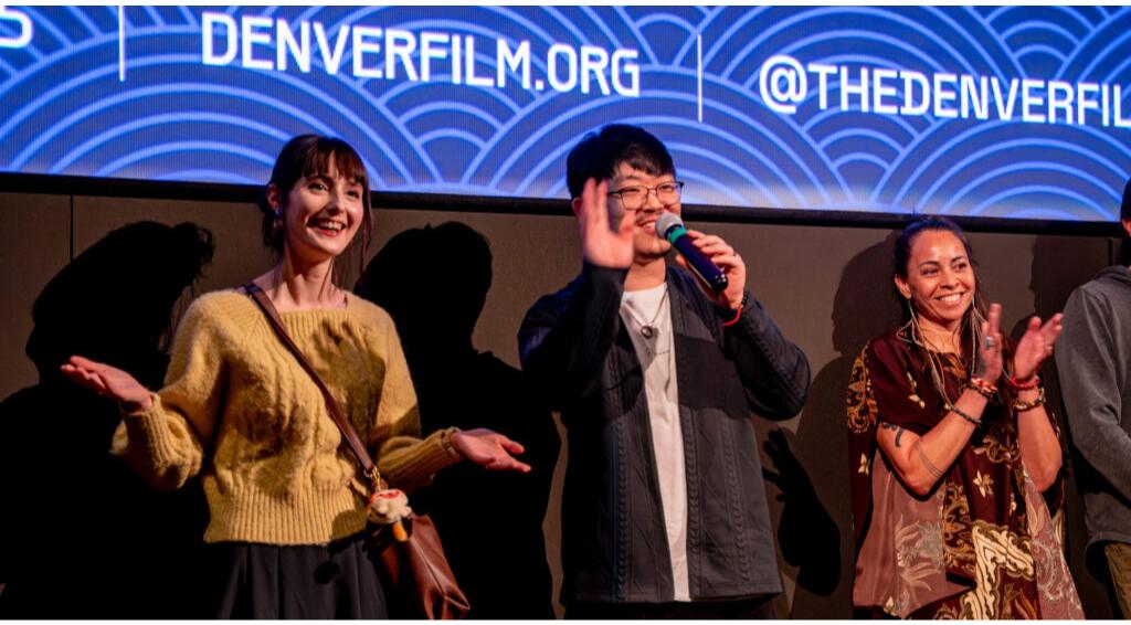 People smiling and waving on stage, "DENVERFILM.ORG @THEDENVERFILM" text above