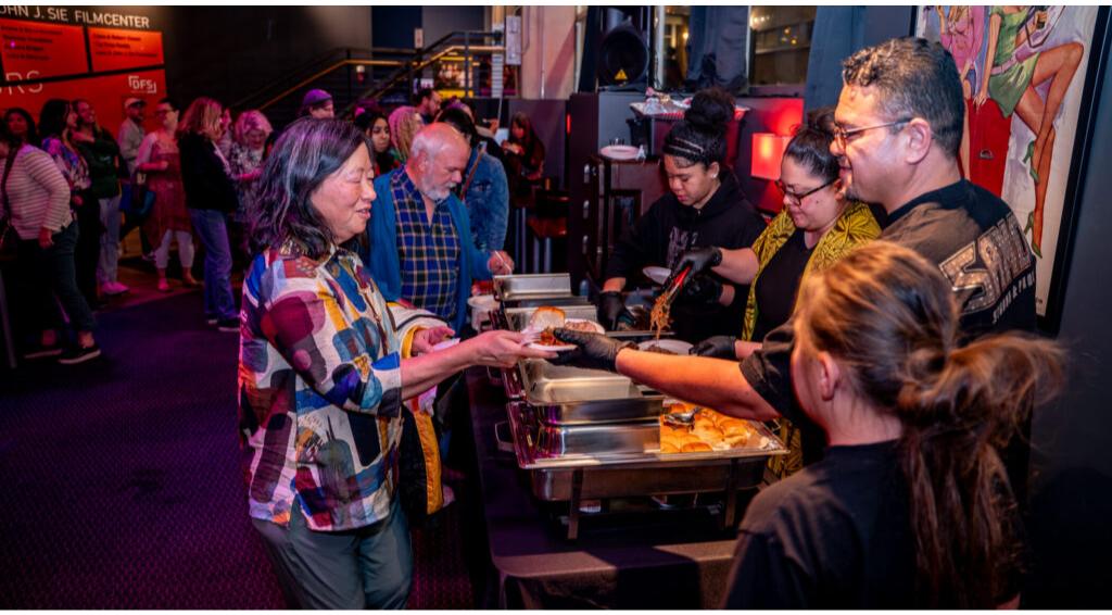 People serving and receiving food at a buffet line in a vibrant setting