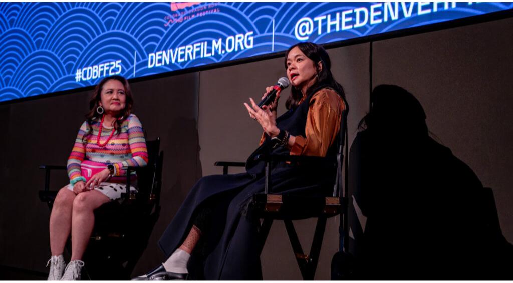 Two women on stage during a panel. One speaks into a microphone. Background screen shows text: "#CDBFF25", "DENVERFILM.ORG", "@THEDENVERFILM"