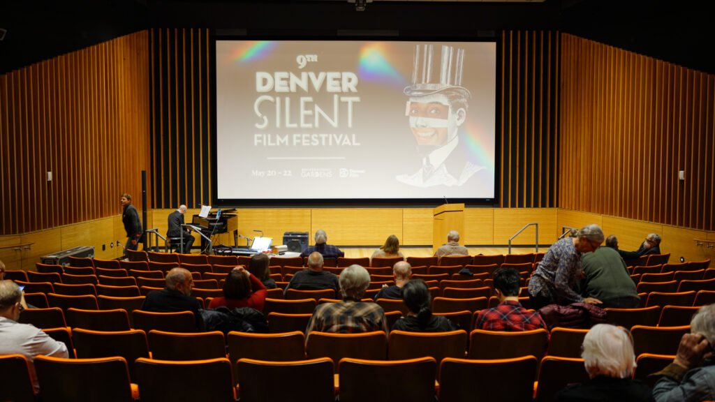 Audience seated in theater for Denver Silent Film Festival, piano player preparing on stage