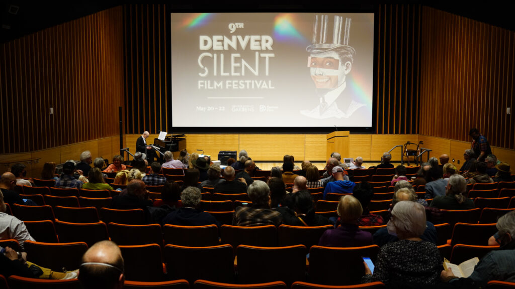 Audience at 9th Denver Silent Film Festival, featuring pianist on stage, large screen display