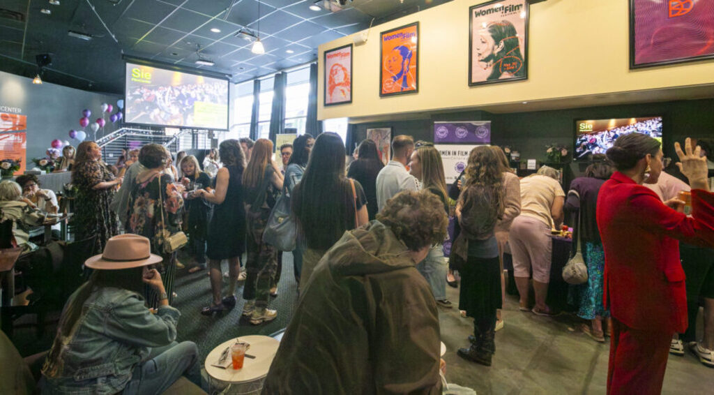 Crowded event at Sie FilmCenter, attendees socializing, surrounded by women-focused posters and decor