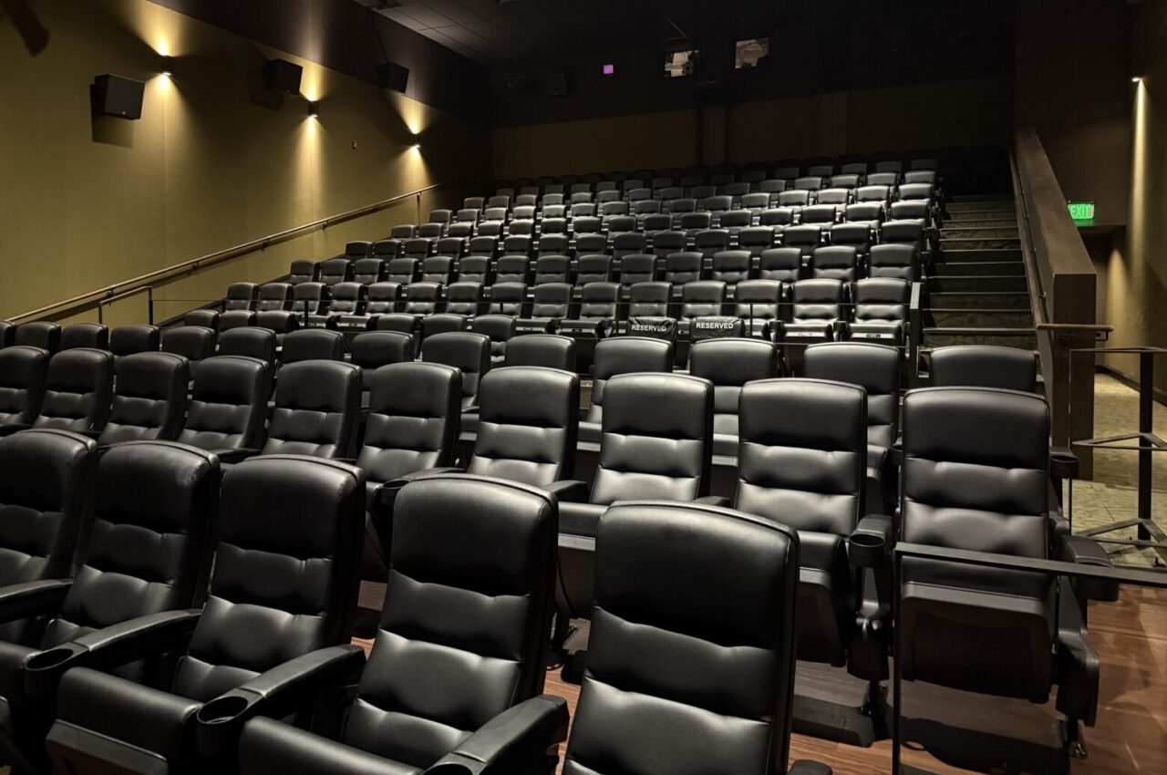Empty movie theater with black seats and "Reserved" signs in the middle row