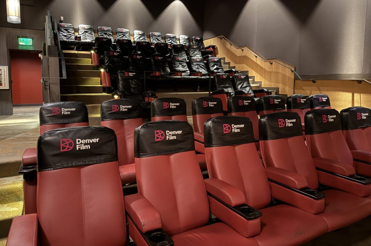 Red theater seats with black headrests labeled "Denver Film" in an empty auditorium