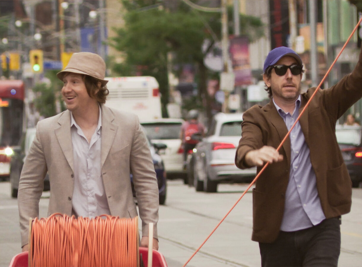 Two men walking down a busy street, pulling orange cable