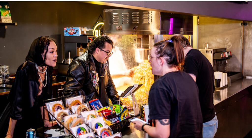 Three people at a snack counter with popcorn machine, engaged in conversation