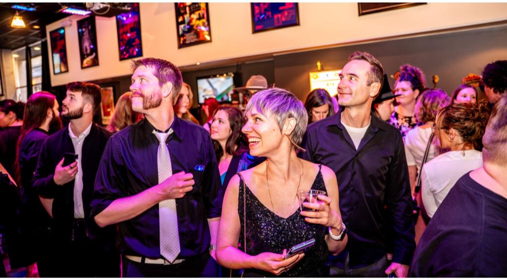A lively party scene with people smiling and socializing under colorful lights