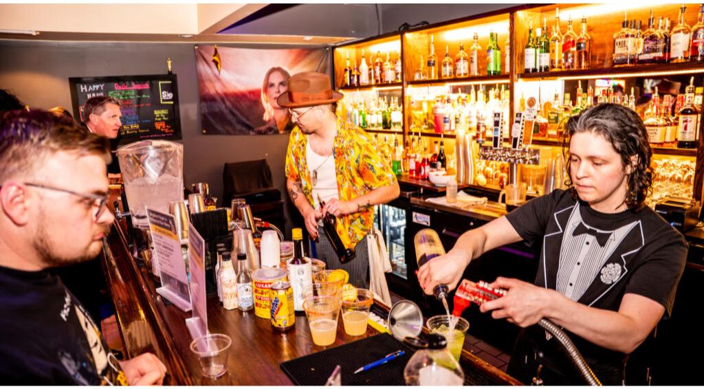 Bartenders serving drinks at a lively bar, colorful shirt, and tuxedo T-shirt, vibrant atmosphere
