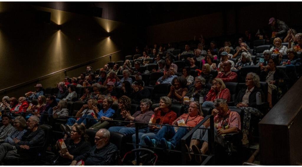 Audience in a dimly lit theater, seated and watching attentively