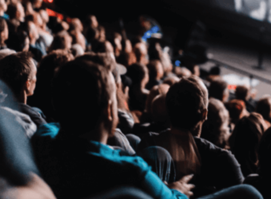 Audience seated in a dimly lit theater, focusing on stage
