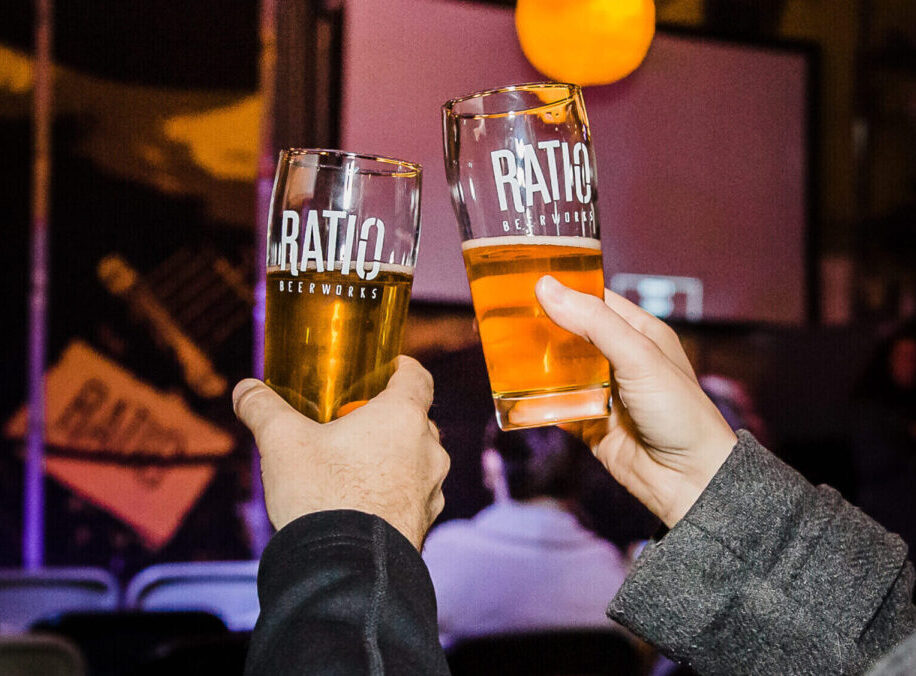 Hands toasting with Ratio Beerworks glasses in a lively setting