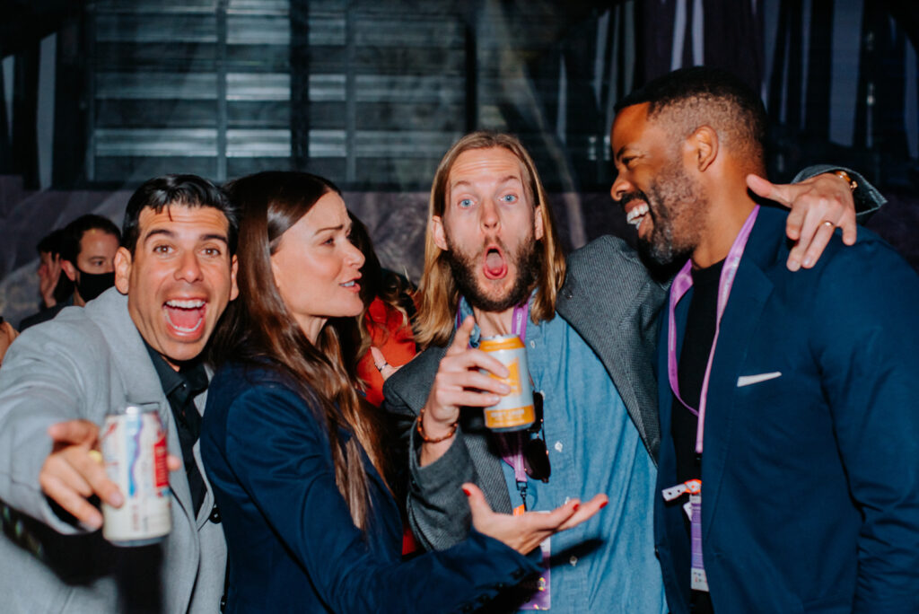 Group of people laughing and socializing, holding drinks, displaying a lively atmosphere