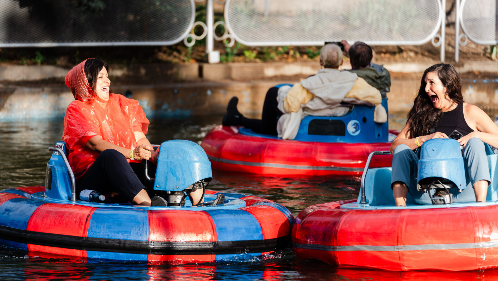 Two women laughing on bumper boats, one in a red poncho