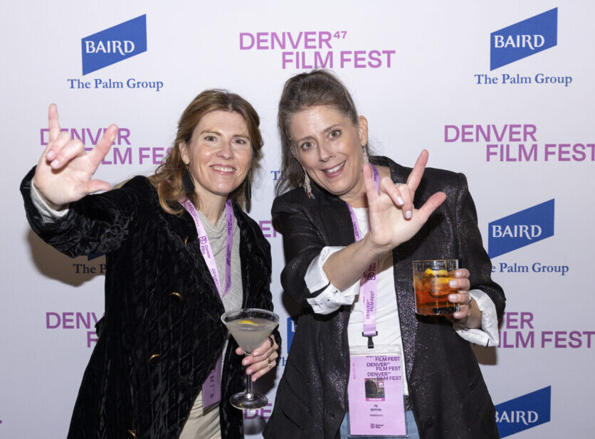 Two women at Denver Film Fest holding drinks, smiling, and gesturing enthusiastically