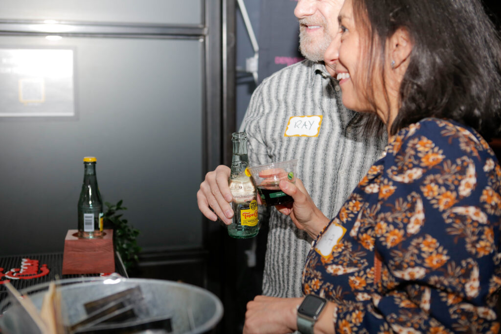 Ray and woman smiling with drinks, wearing name tags at casual gathering