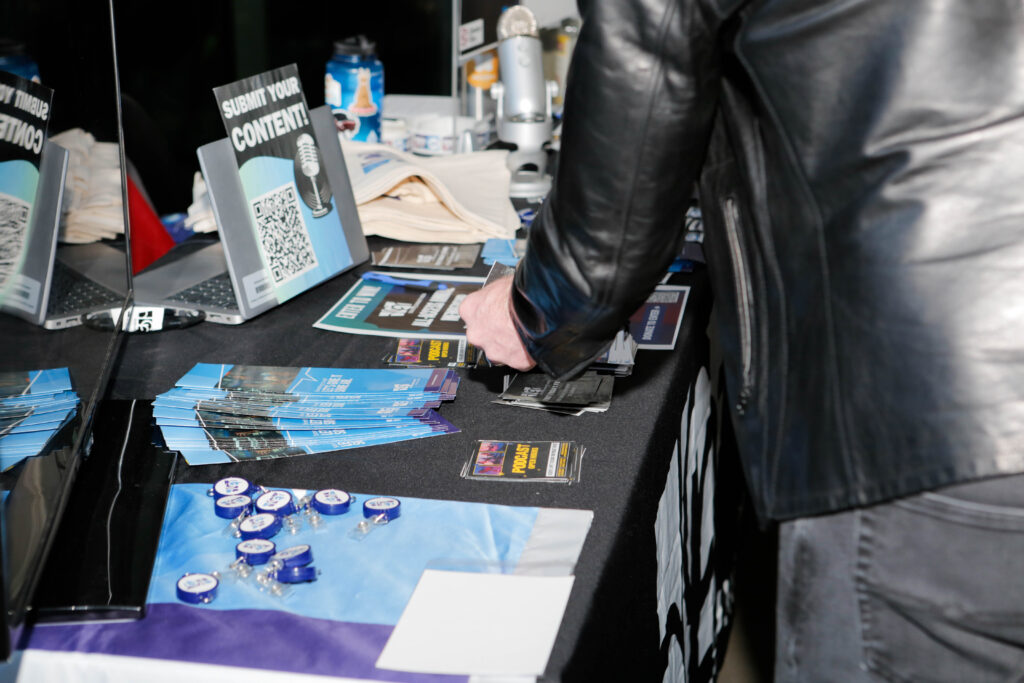 Person at a table arranging flyers and "Submit Your Content!" signage with QR code