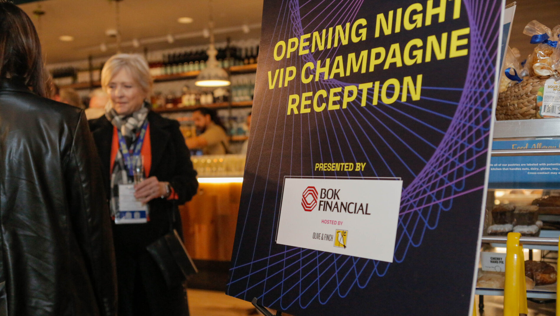 Sign for "Opening Night VIP Champagne Reception" by BOK Financial, hosted by Olive & Finch, in a bustling venue