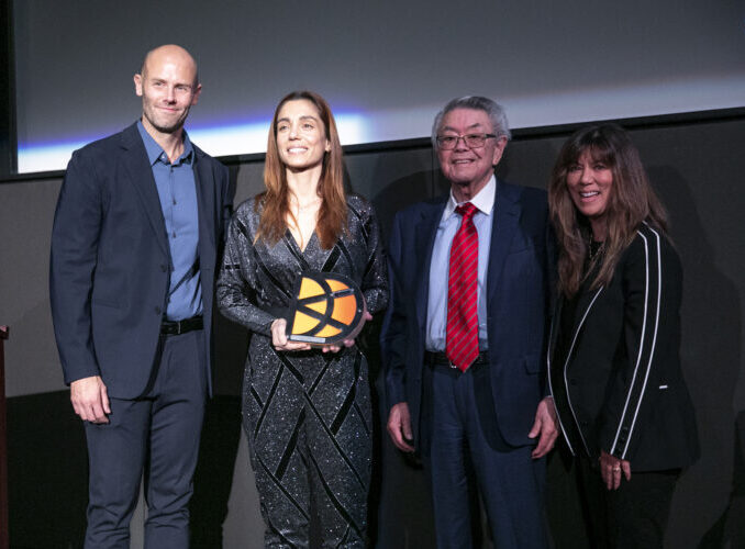 Christiana Dell’Anna holding an award, standing with three smiling people on stage