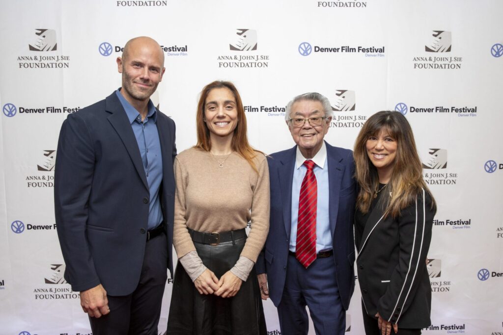 Christiana Dell'Anna with others at Denver Film Festival, smiling in front of sponsor backdrop