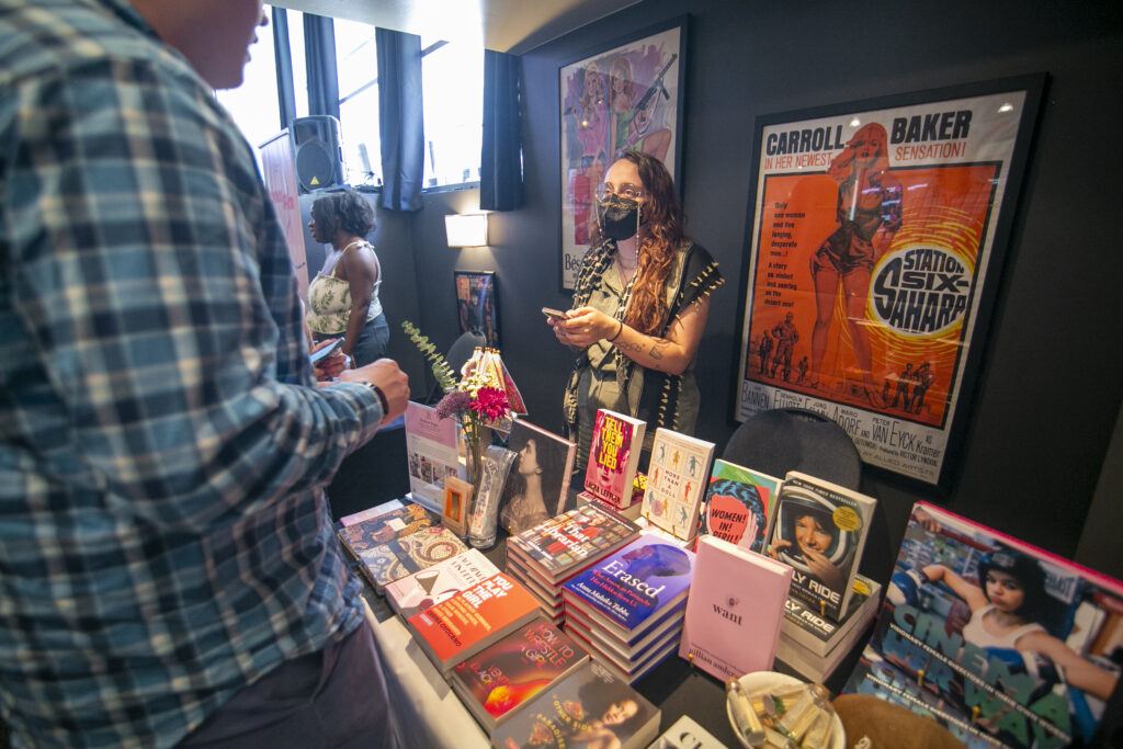 DeWitt Marketplace scene with people browsing a table filled with books and colorful posters on the wall