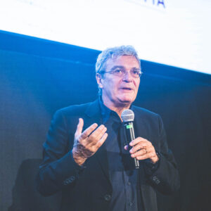 DeWitt speaking on stage, holding a microphone, with an expressive gesture