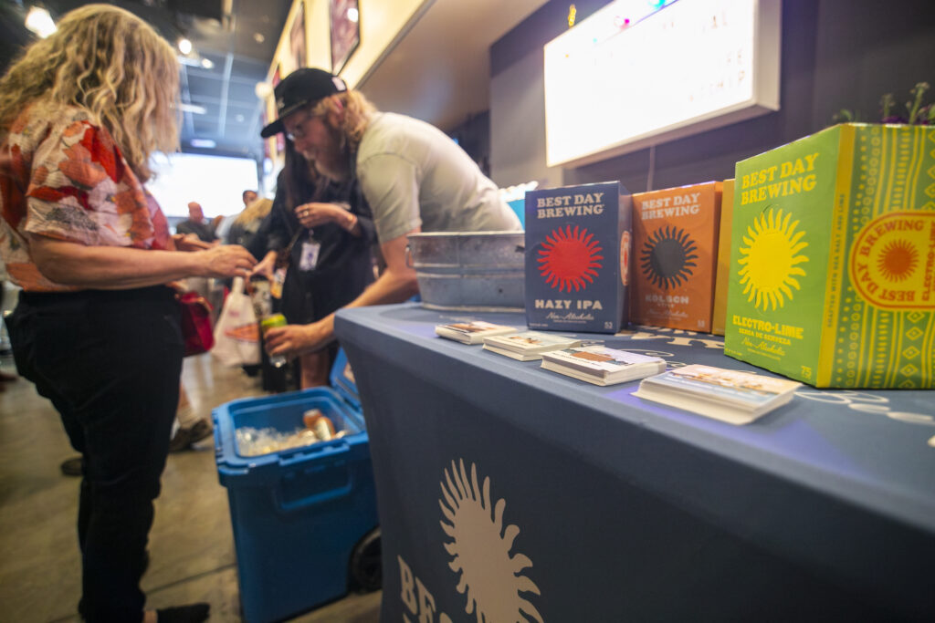 People interacting at an event table with "Best Day Brewing" boxes
