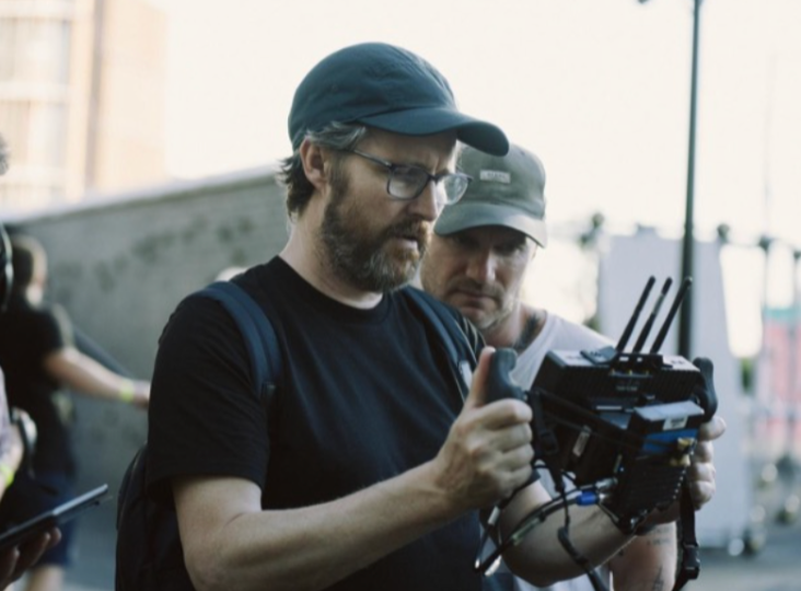 Man in cap examining film equipment, surrounded by crew on set