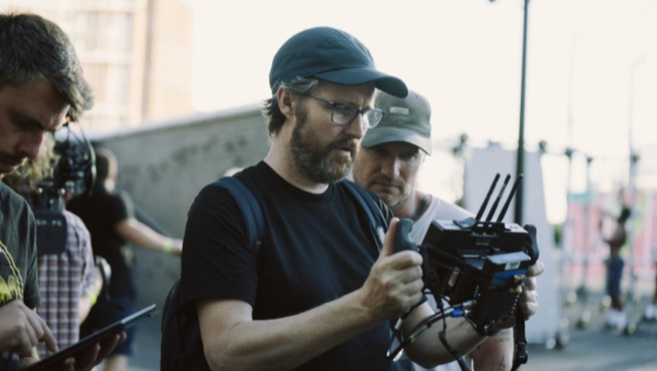 Man in cap examining film equipment, surrounded by crew on set