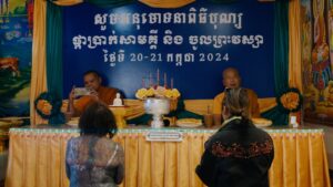 Two monks sit at a decorated table, blue background text reads: "សូមសរសើរព្រះសង្ឃ ២០-២១ កក្កដា ២០២៤"