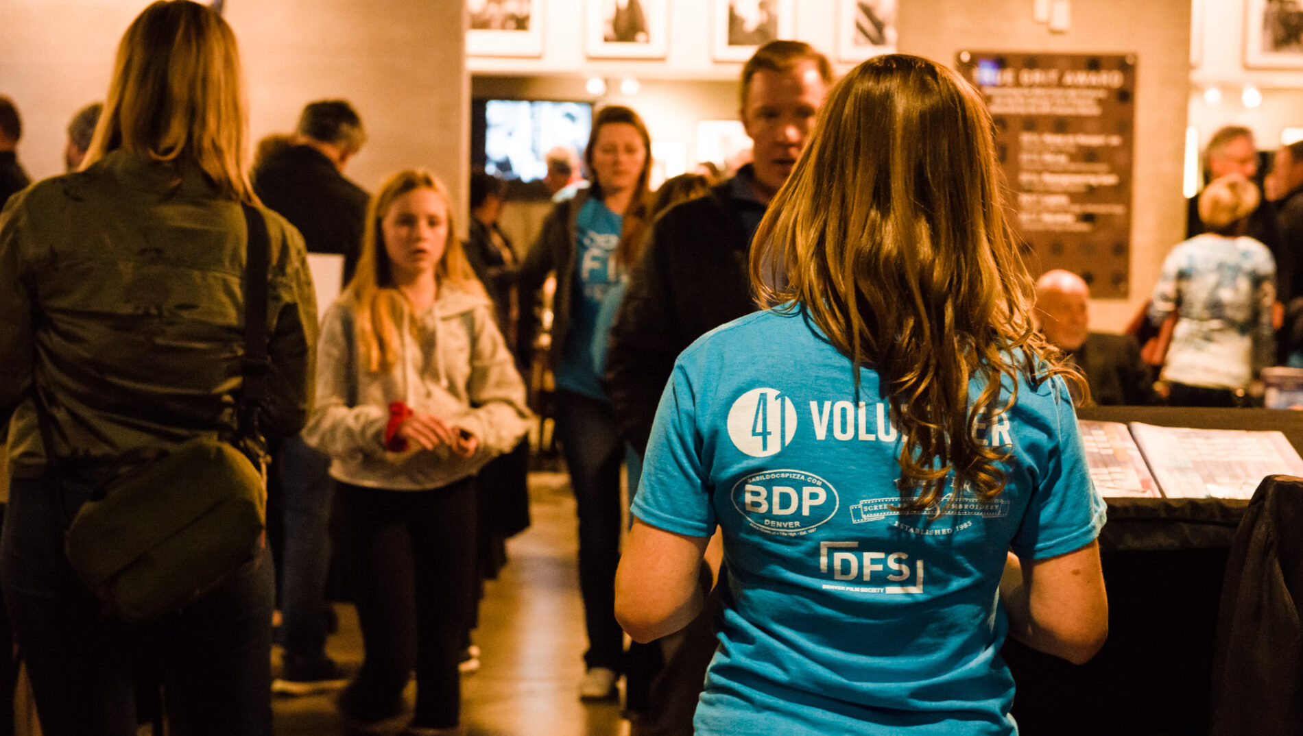 Katie-Leigh, venue volunteer in blue shirt, attends an event with attendees in the background