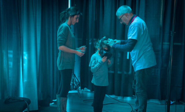 Katie Leigh assists a child with a VR headset, blue-lit room