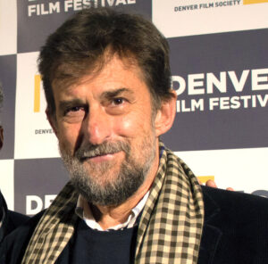 A person smiling at the Denver Film Festival backdrop, wearing a checkered scarf