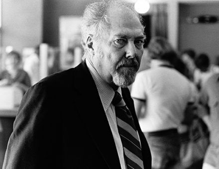 Robert with a serious expression, wearing a suit and tie in a busy setting