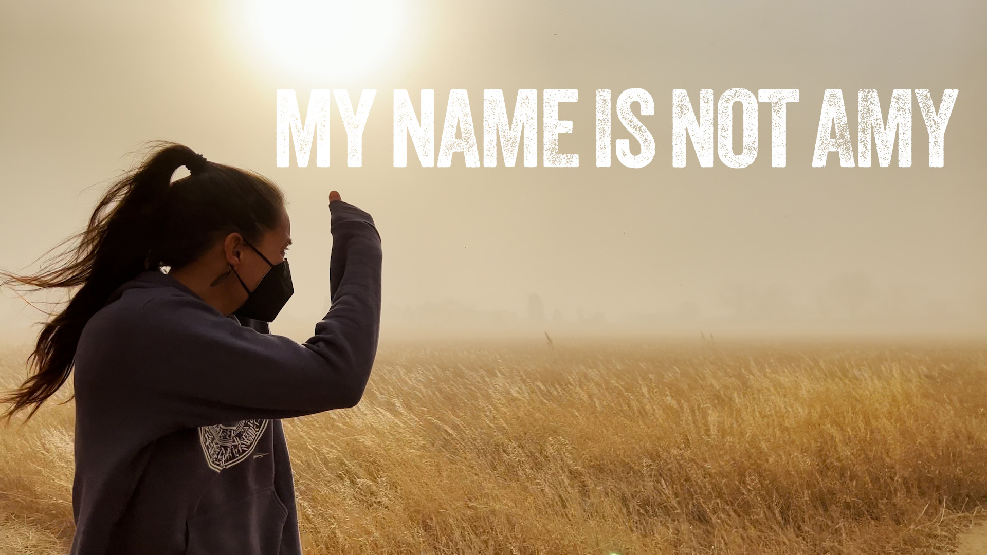 Person in field wearing mask with text "My Name Is Not Amy" in sunlight