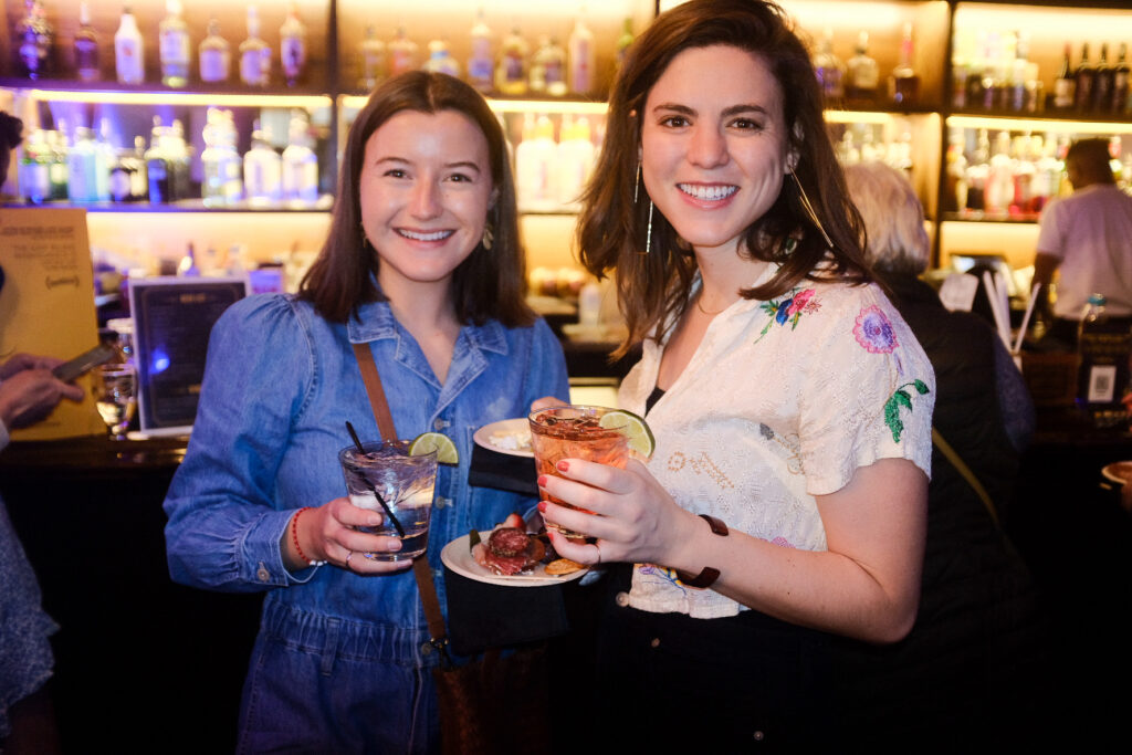 Women in bar holding drinks and snacks, smiling happily