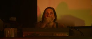 Woman covering mouth in surprise, dimly lit room, tense atmosphere