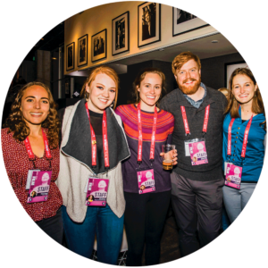 Five people wearing event lanyards, smiling in a group at a gathering