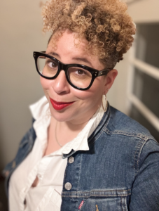 Summer smiling with glasses, curly hair, bold lipstick, denim jacket, and white shirt