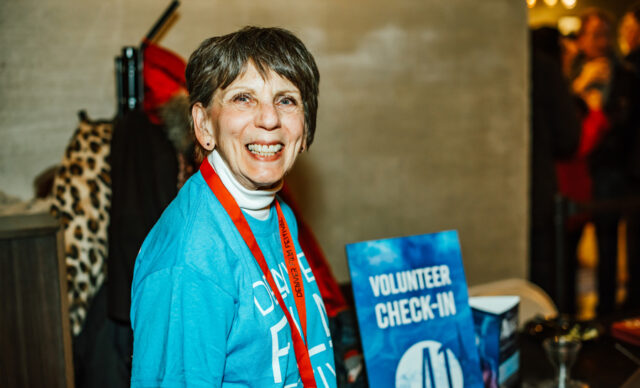 Support-Volunteer-3.jpg smiling at volunteer check-in table wearing blue shirt and red lanyard