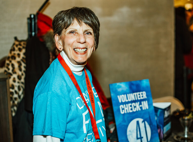 Support-Volunteer-3.jpg smiling at volunteer check-in table wearing blue shirt and red lanyard