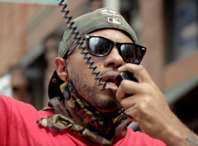 The-Holly-Still.jpg: Person wearing sunglasses using a megaphone during a protest