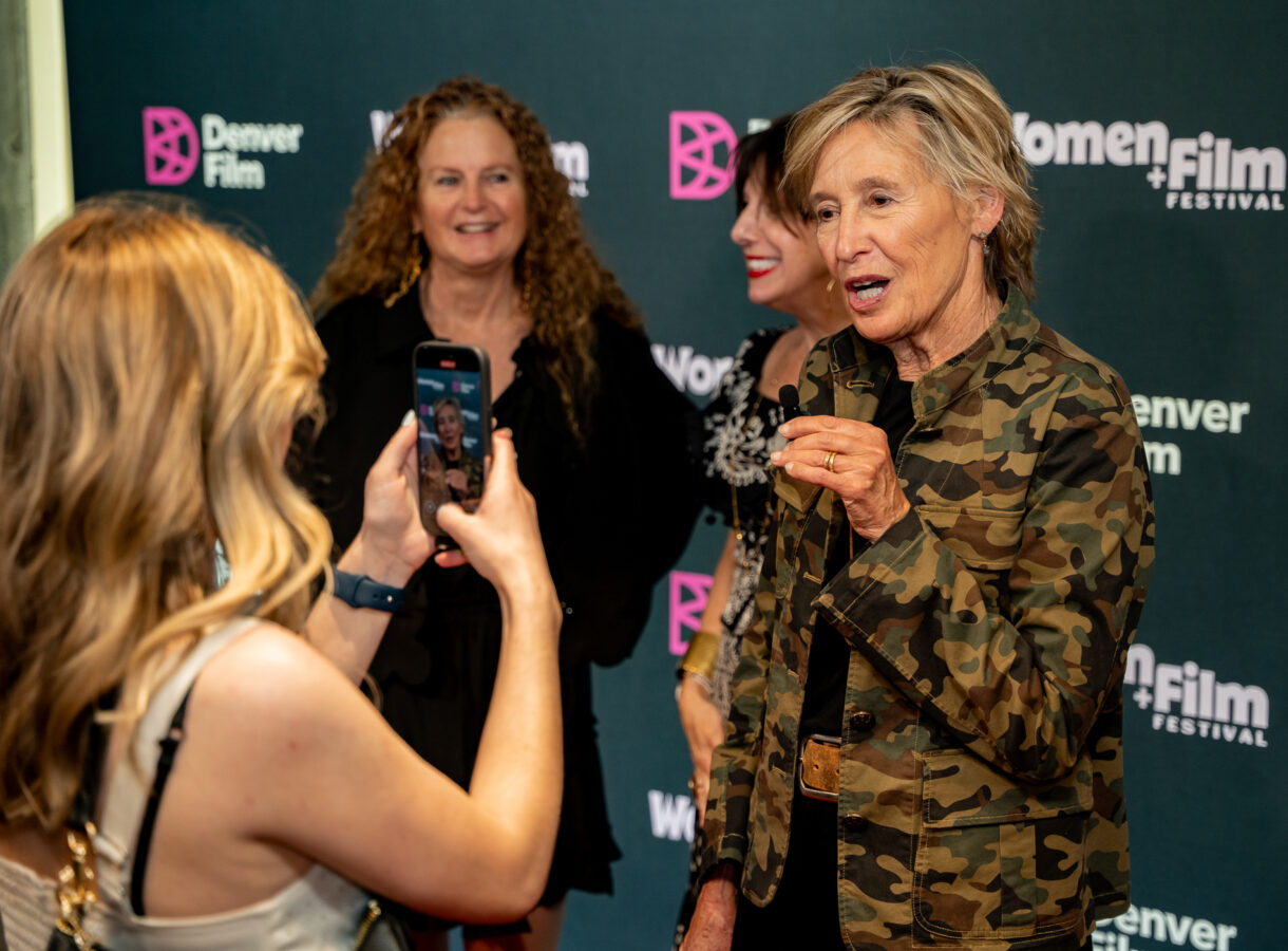 Woman in camouflage jacket speaking at Women+Film Festival event, photographed by audience member