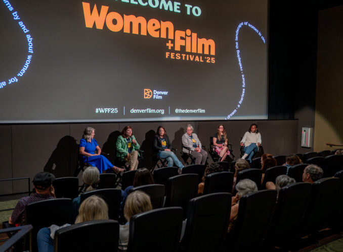 Panel discussion at Women+Film Festival '25 with five speakers in front of an audience, film festival branding visible