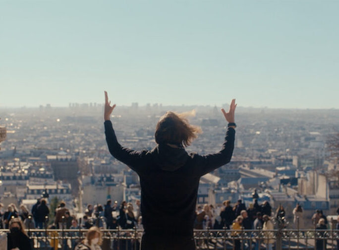 Rear view of a person with raised arms facing a cityscape, viewed between two stone columns