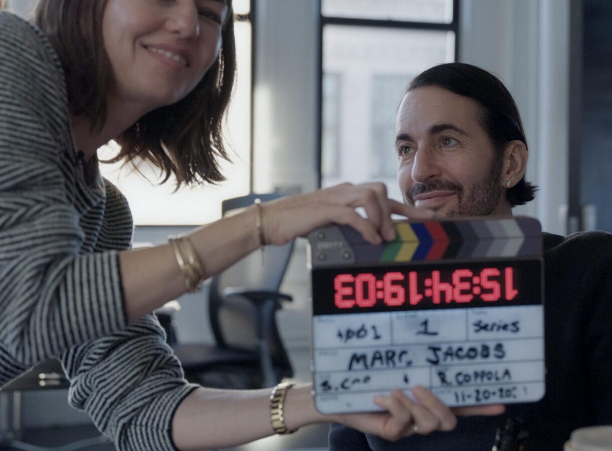 Marc smiling behind a film clapperboard reading "Series Marc Jacobs," held by a woman