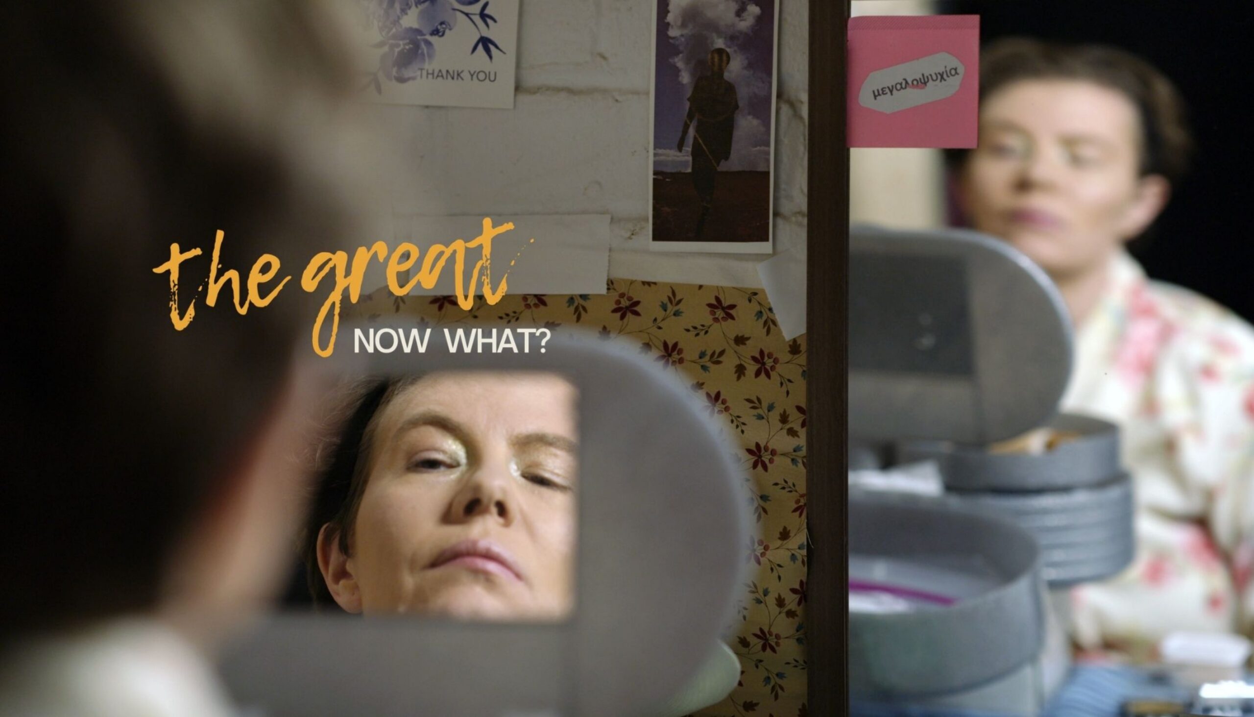 A person reflected in a mirror, text reads "the great NOW WHAT?" with makeup items visible nearby